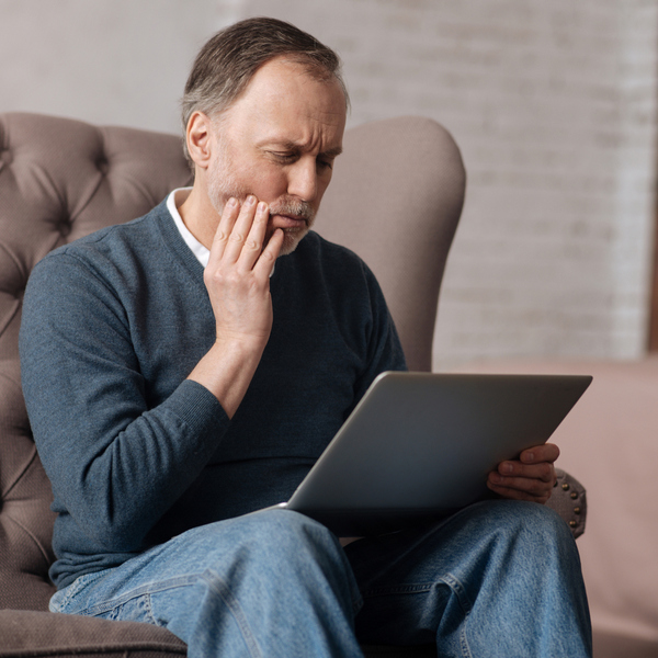 Senior man with toothache looking at laptop in the chair